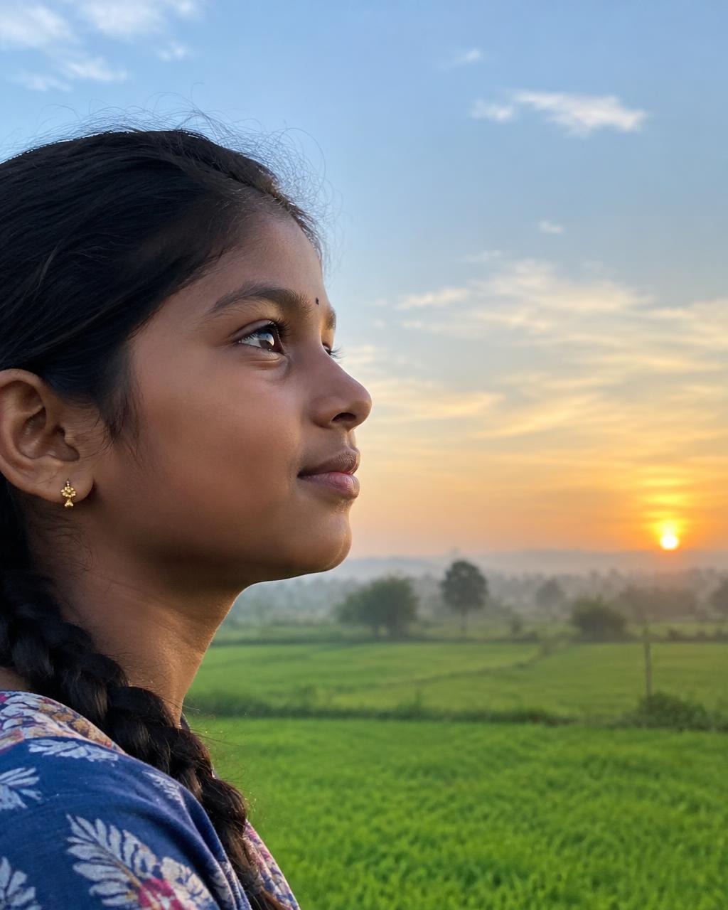 Illustrative image: a girl looking toward a sunrise over green fields